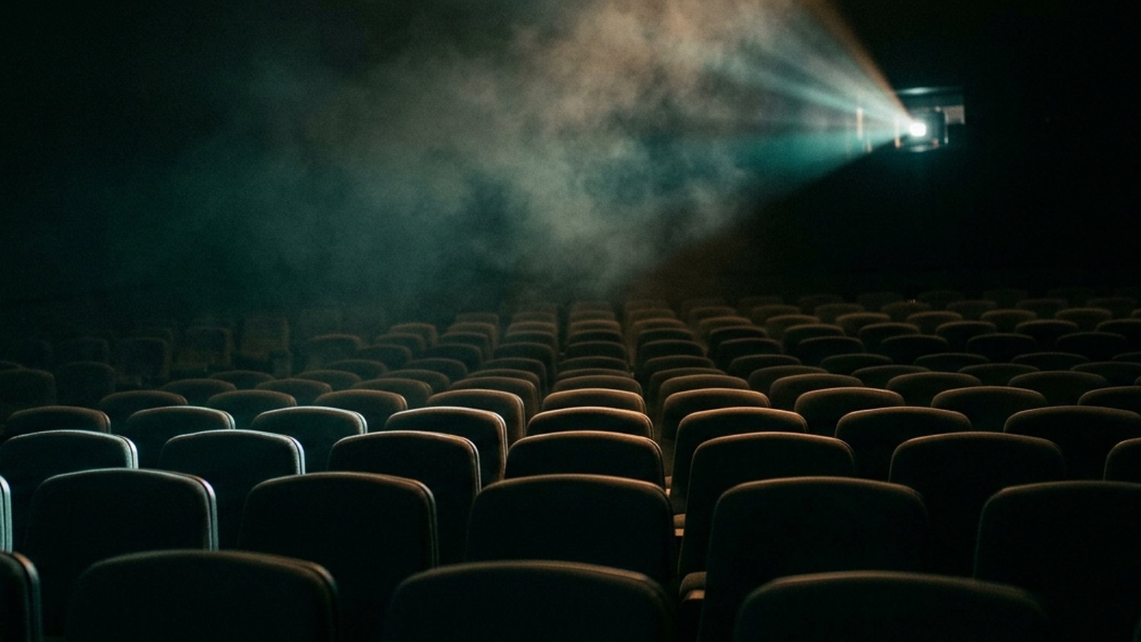 Empty cinema seats in a dark auditorium lit by a single projector beam